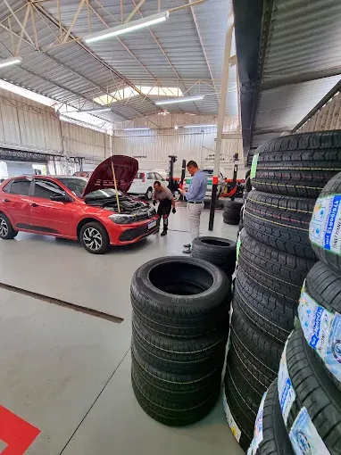 Carro vermelho no galpão da oficina ao lado de uma pilha de pneus novos
