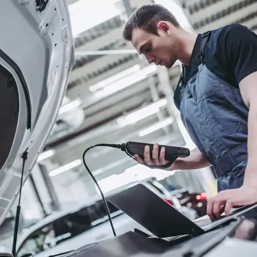 Mecânico conectando um scanner e um notebook ao carro para o diagnóstico da injeção eletrônica