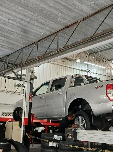 Mecânico trabalhando sob uma picape prateada elevada na oficina