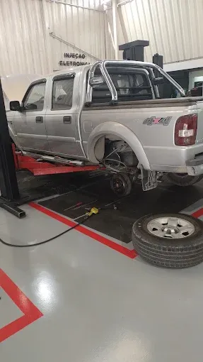 Picape elevada na oficina com a roda removida e o pneu apoiado no chão