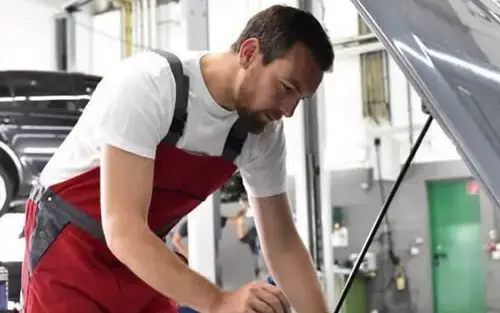 Mecânico inspecionando o motor de um carro com o capô aberto durante a revisão