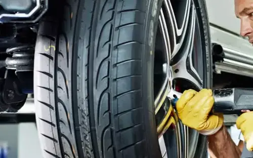 Mecânico de luvas amarelas trocando o pneu de um carro com ferramenta pneumática